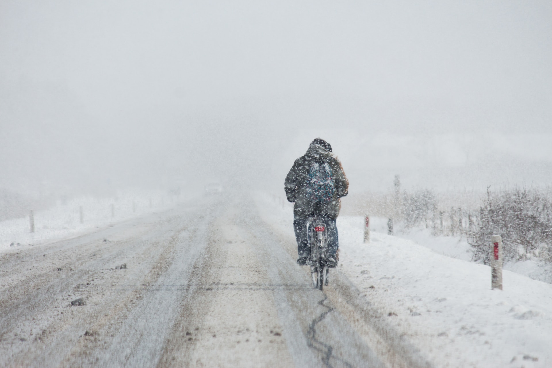 lonely-scene-of-dutch-cyclist-biking-down-a-road-covered-in-snow-as-fresh-snow-falls-around-them